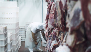 Carnes penduradas dentro de frigoríficos com açougueiro ao fundo