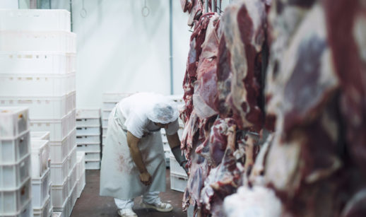 Carnes penduradas dentro de frigoríficos com açougueiro ao fundo