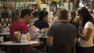 Grupo de pessoas reunido em mesa no Mercado Municipal de SP analisando preços, alusivo à inflação de junho