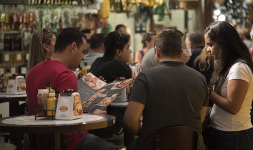 Grupo de pessoas reunido em mesa no Mercado Municipal de SP analisando preços, alusivo à inflação de junho