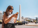 Turista brasileira mexendo no celular em frente ao Obelisco de Buenos Aires, onde o real ganhou poder de compra