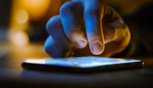 Close de mão de pessoa digitando na tela de celular ligado, alusivo a golpes via aplicativos de mensagens