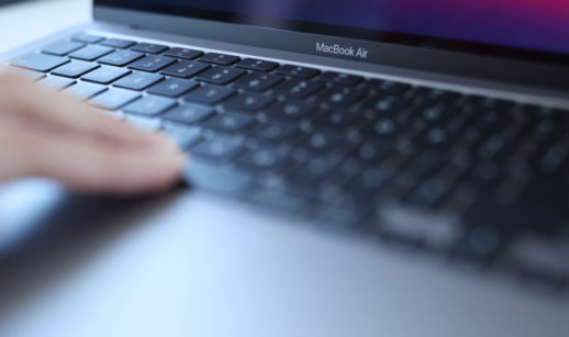Close de mão tocando teclado de MacBook Air, da Apple, na cor cinza