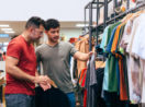 Dois homens de camisa cinza e vermelha mexendo em arara de lojas de roupas, alusivo às vendas nos shoppings da Multiplan