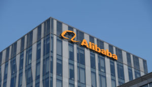 Perspectiva de baixo para cima de prédio espelhado do Alibaba, com sede na China, com destaque para o logo da empresa em laranja
