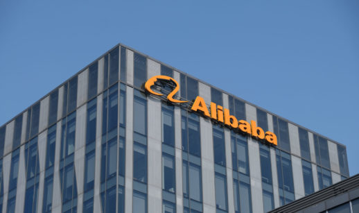 Perspectiva de baixo para cima de prédio espelhado do Alibaba, com sede na China, com destaque para o logo da empresa em laranja