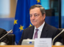 Mario Draghi, de terno preto e gravata roxa, sorrindo de boca fechada e bandeira da União Europeia em segundo plano
