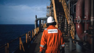 Funcionário da PetroRio, que emitirá debêntures, de costas com macacão laranja dentro de plataforma de petróleo