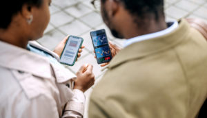 Casal de costas olhando para telas de celulares com gráficos de mercado financeiro, alusivo ao investimento na carteira Safra Top 10 Ações