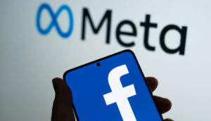 Tela de celular aberto com o logo gigante do Facebook e, atrás, o logo da Meta, que fez acordo para encerrar o caso da Cambridge Analytica