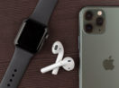 Mesa de madeira escura com Apple Watch, AirPods e iPhone expostos, alusivo ao lançamento do modelo 14 do celular