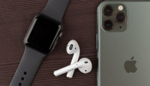 Mesa de madeira escura com Apple Watch, AirPods e iPhone expostos, alusivo ao lançamento do modelo 14 do celular