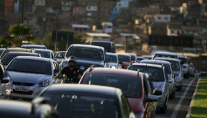 Tráfego de veículos em Salvador, na Bahia, com pôr do sol e casas bem ao fundo, alusivo ao volume de financiamento de veículos