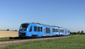 Trem da Alstom movido a hidrogênio que está na Alemanha na cor azul, em trilho com céu azul e gramado verde no entorno