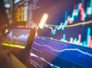Close de telas com gráficos do mercado financeiro em celular e computador, alusivo à oscilação das ações do Hapvida