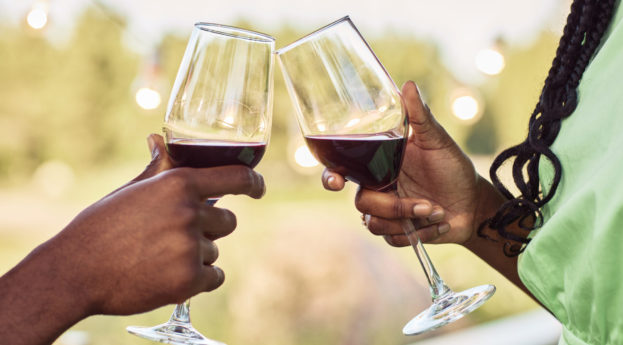 Close de mãos de casal brindando taças com vinho tinto dentro