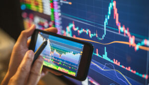 Investidor analisa gráfico no celular e em uma tela de computador