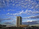 Prédios do Congresso Nacional, em Brasília, onde tramita a reforma tributária, com céu azulado cheio de nuvens granuladas