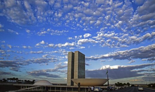 Prédios do Congresso Nacional, em Brasília, onde tramita a reforma tributária, com céu azulado cheio de nuvens granuladas