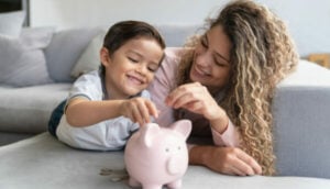 mãe e filho colocando uma moeda no cofre, alusivo a educação financeira infantil