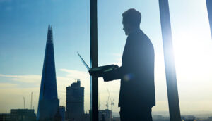 Executivo com laptop em mãos olhando para paisagem de cidade, alusivo ao processo de alavancar o escritório de investimentos
