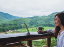 Jovem mulher com computador em varanda nas montanhas, alusivo às finanças sustentáveis