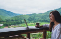 Jovem mulher com computador em varanda nas montanhas, alusivo às finanças sustentáveis